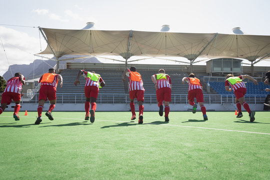 Rear view of hockey players running before match on pitch