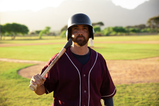 Baseball player looking at camera holding a baseball bat and a helmet