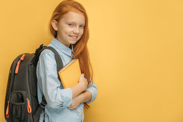 side view on beautiful red haired school girl isolated over yellow background. sweet little girl...