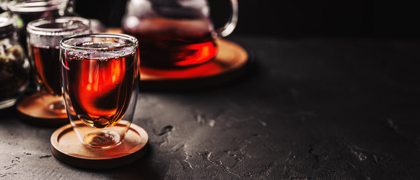 Cup of freshly brewed black tea, dark moody, tea ceremony. Hot water is poured from the kettle into a flass cup on wooden tray, black concrete background,space for text.