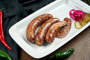 Appetizing juicy pork minced sausage grilled in a smoker with cheddar in a white plate with canned vegetables. German beer snack