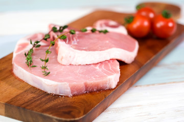 Two pieces of fresh raw pork steak with tomatoes, thyme on dark wooden. Raw pork is ready to cook. Food and kitchen concept