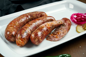 Appetizing juicy pork minced sausage grilled in a smoker with cheddar in a white plate with canned vegetables. German beer snack