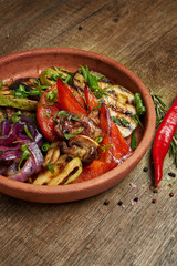 Assorted grilled vegetables - mushrooms, zucchini, peppers, corn in a ceramic plate on a wooden background. Vegetarian warm salad. Healthy food