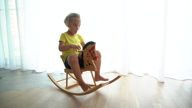 Mad 5 years old girl simper riding wooden rocking horse at home. camera motion