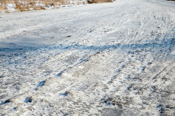 Dangerous driving conditions. Icy road with tracks from the wheels of cars . The concept of safe driving on a winter slippery track. The texture of the ice road.