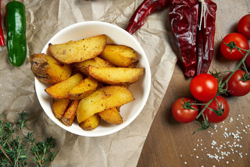 Baked potatoes in spices in a white bowl in a composition with vegetables and specialty. Recipe photo