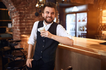 young happy bearded waiter laughing, looking up, holding smoothie, close up side view photo.awesome flavor