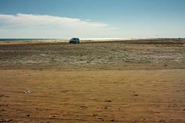 A car runs along the lonely and windy beach by the sea.