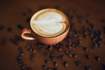 Coffee cup with heart in coffee shop, top view close up photo.cappuccino in pink cup with latte art and roasted coffee beans on wooden table blurred background