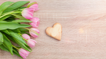 Rosarote Tulpen auf einem hellen Holztisch  mit Holzherz