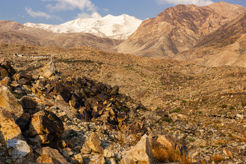 Obraz premium A snow capped Himalayan peak towering over the rocky slopes of the dry, barren mountains in the village of Nako in Kinnaur in Himachal Pradesh, India.