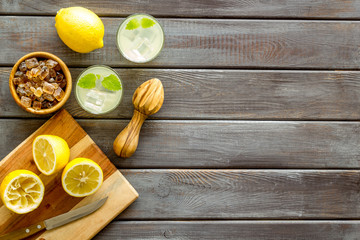 Homemade lemonade in glasses near juicer and cut lemons on wooden background top-down copy space