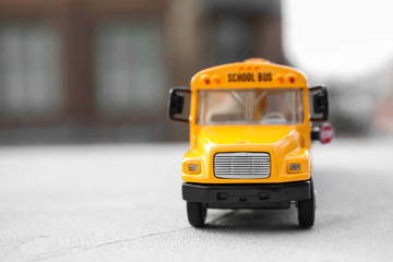 Yellow toy school bus against blurred background, space for text. Transport for students