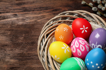 Obraz na płótnie Canvas Colorful Easter eggs in decorative nest on wooden background, closeup. Space for text