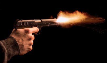 The hand presses the trigger of the gun and the flame from the shot escapes from its muzzle - 329129350