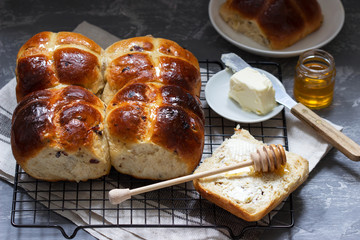 Traditional hot cross buns with honey and butter on a concrete background.