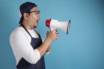 Young Asian male chef or waiter speaking on megaphone, advertisement concept