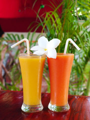 Two glass glasses with freshly squeezed juice and frangipani flower