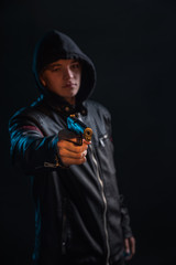 a bandit in a hood and leather jacket with a gun in his hand in the lights of the night city