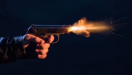The hand presses the trigger of the gun and the flame from the shot escapes from its muzzle - 329129913