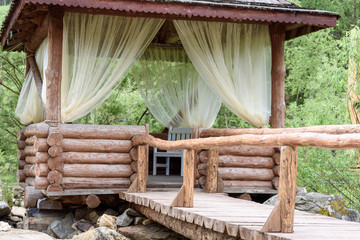 Summer gazebo with white curtains for relaxation and entertainment in the forest.