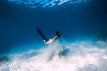 Freediver girl with fins glides over sandy sea bottom in ocean.