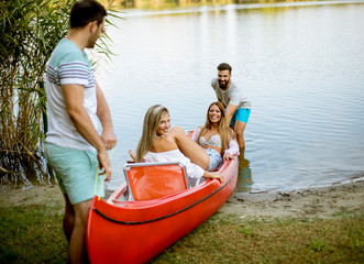 Obraz premium Young men pulling canoe with young women into calm lake