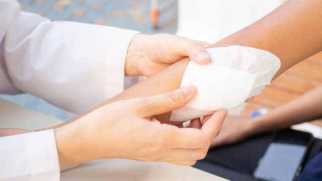 Doctor is using cotton dressing a wound at a women arm.