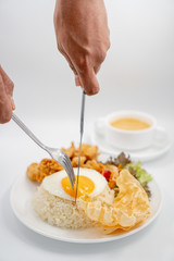 Buttermilk chicken rice with ingredients isolated on white with fried egg and salad. Fork and knife cut the fried egg.
