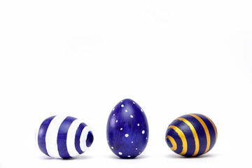Three easter eggs trendy colored classic blue, white and golden decorated on white table. Happy Easter card with copy space for text. Minimal style.