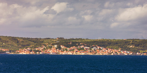 Fototapeta premium Supetar city in Brac island, Croatia. View from the sea. Picturesque scenic view on Supetar on Brac island, Croatia. Panoramic view on harbor of town Supetar from the side of sea. Brac, Croatia.