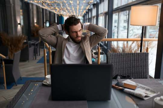 Stressed disappointed guy has bad wifi connection in coffee shop while performing work.Angry businessman shocked with company web site failure browsing page on laptop computer, close up photo