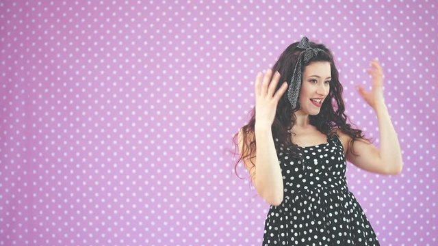 Kinky brunnete girl in nice black polka-dot dress readjusting her hairdo, smiling pleasantly.