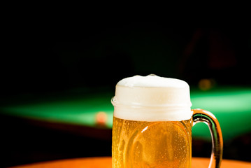 Mug with draft beer on a table with pool table behind