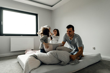 Naklejka premium people, family and morning concept - happy child with parents having pillow fight in bed at home,family with a funny pillow fight on the bed. Parents spend their free time with their daughters.