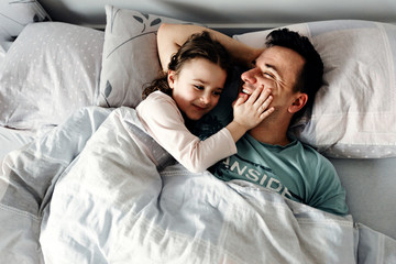 Fototapeta na wymiar dad and daughter are smiling and smiling joyfully,father with a child after sleep fooling around in pajamas,dad tickles baby,a happy family,dad with daughter in the morning