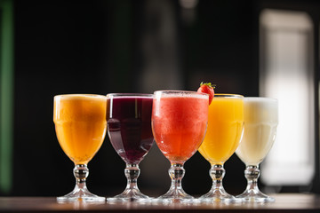 bowls of natural juices, passion fruit, grape, strawberry, orange, pineapple, on a table with dark background