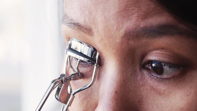 Young Asian model's face during the Make-Up process. Lash curling with a lash curler on a wedding day. 4k video