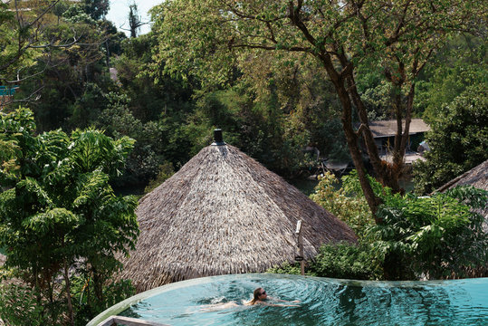 Woman In Swimsuit And Sunglasses Relaxing In Luxury Infinity Pool With Jungle View