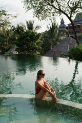 Fototapeta premium Woman in swimsuit and sunglasses relaxing in luxury infinity pool with jungle view