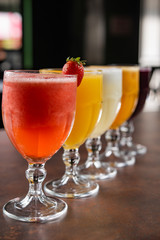 bowls of natural juices, passion fruit, grape, strawberry, orange, pineapple, on a table with dark background