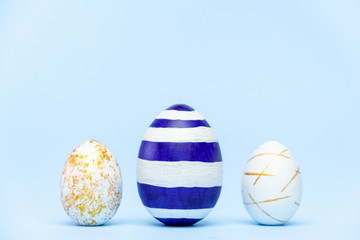 Three easter trendy colored classic blue and golden decorated eggs on blue background. Happy Easter card with copy space for text. Minimal easter style.