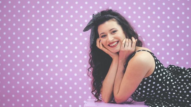Enticing kinky brunnete girl in beautiful polka-dot dress lying on her belly on the bench, giving an airkiss.