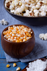 Unpopped corn kernels for making popcorn in a wooden cup on blue table