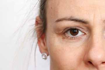 Macro shot of upper female face with open brown eye and no make up against a plain light background