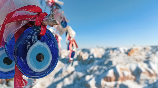 Evil eye charms hang on the tree with snow covered fairy chimneys landscape in Cappadocia, Turkey.