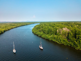 An aerial shot of two sailboats anchored on the middle of a natural mangrove canal in the...