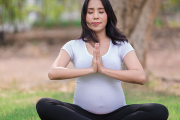 Fototapeta premium Portrait of asian Beautiful pregnant woman at the park,Thailand people,Happy woman concept,Her play yoga on the lawn