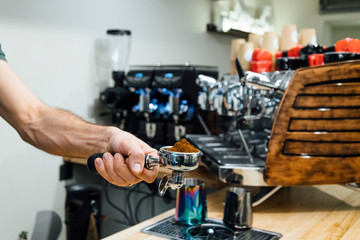Fototapeta na wymiar Detail of man hand holding portafilter recipient filled with coffee ground while preparing espresso